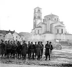 Des hommes en arme sur une place de la ville, avec des bâtiments en arrière-plan.