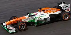 Photographie d'une monoplace de Formule blanche, orange et verte, vue de profil, de haut.