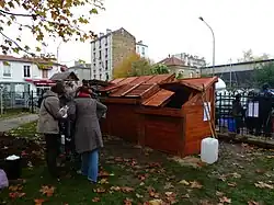 Pavillon de compostage de quartier du Square de la Place de la République à Montreuil (Seine-Saint-Denis), inauguré le 26 novembre 2011, avec l'association « Le Sens de l'Humus ». Deux compartiments (1,7&nbsp;m3 chacun) pour les résidus végétaux et un compartiment de réserve (1&nbsp;m3) contenant du bois raméal fragmenté et un réservoir de récupération de l'eau de ruissèlement. Bois de récupération (palettes). Éléments démontables. Réalisé par des Roms dans le cadre d'un projet d'insertion. Financement : ville de Montreuil. Photographie : ville de Montreuil (cliquez sur l'image).