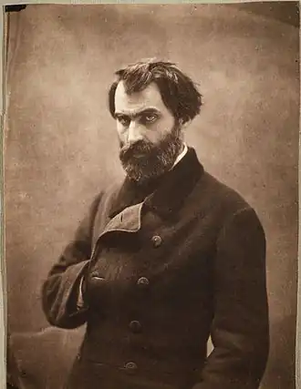Photographie sépia d’Eugène Pelletan, homme brun au regard perçant, tête nue, portant la barbe, la main droite glissée dans sa redingote à la manière de l’empereur Napoléon 1er.