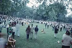 Photo en couleur d'une foule réunie dans un parc arboré
