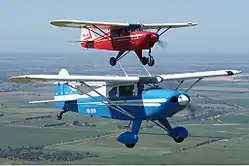 Piper Tri-Pacer ; le bleu, en avant-plan, est conforme à sa représentation dans l'album (roulette sur béquille de queue, et non sur jambe à l'avant).