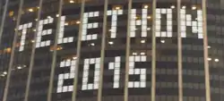 De petits caractères de texte en pixel art sur les fenêtres de la Tour Montparnasse lors d'un Téléthon