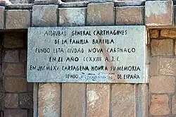 Plaque blanche avec des lettres noires en majuscule mentionnant Hasdrubal comme le fondateur de Qart Hadasht (aujourd'hui Carthagène)