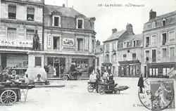 Carte poste en noir et blanc présentant la place Henri IV au début du XXe siècle : des marchandes des quatre-saisons devant la statue, les raisons sociales des magasins peintes sur les murs, un timbre oblitéré en bas à droite.