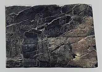 Plaque en ivoire de style assyrien (noircie par un incendie) représentant des porteurs de tribut. Nimroud, temple de Nabû, IXe&nbsp;– VIIIe&nbsp;siècle av. J.-C. Metropolitan Museum of Art.
