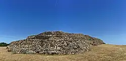 Vue de trois-quarts de l'ensemble du cairn, proue en premier plan. À la proue, on remarque la série de grosses dalles verticales du parement médian.