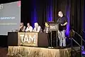 Novella (au milieu) dans 2015, sur le panneau podcast de TAM13. Son frère Jay est assis deuxième de la droite.