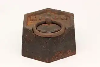 Un poids d'un kilogramme de qualité domestique en fonte grise. Sa forme suit la recommandation R52 de l'OIML pour les poids hexagonaux en fonte grise.