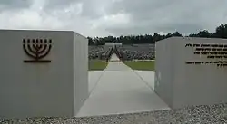 Inscriptions en hébreu, en polonais et en anglais sur un mur en pierre blanche. La base du mur présente de longues stries verticales comme s'il avait été griffé.
