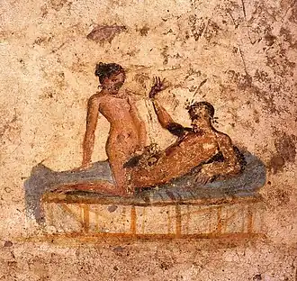Peinture sur un mur montrant une femme blanche chevauchant sexuellement un homme allongé sur un lit ou une banquette.