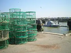 Des casiers de pêche sur un quai du port d'Ouistreham avec, en arrière-plan, la vedette de la Gendarmerie maritime.