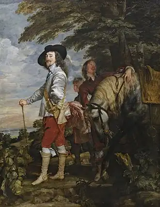 Charles Ier portant une veste grise, un pantalon rouge, des bottes, une canne et un chapeau noir et une tenue d'équitation se tient sous un arbre aux côtés d'un cheval et de son écuyer.