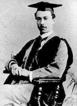 Photographie en noir et blanc d'un jeune homme assis dans une attitude digne, arborant le mortarboard académique de la remise des diplômes dans les pays anglo-saxons.