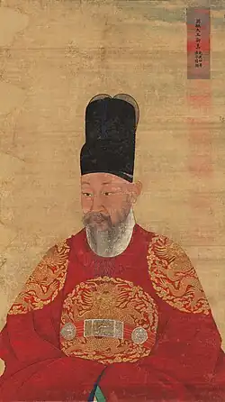 Dessin montrant un homme vêtu d’une robe rouge à broderie de dragons dorés sur la potrine et les épaules et d’un haut chapeau noir.