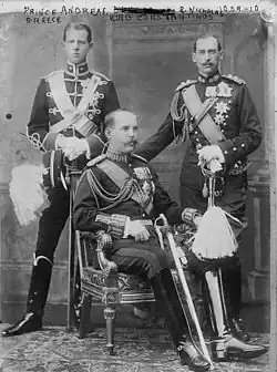 Photographie en noir et blanc montrant trois hommes en uniforme militaire. Celui du milieu est assis et de trois-quart, les deux autres sont debout et de face.