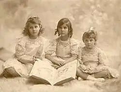 Trois petites filles assises en tailleur avec, devant elles, un grand livre.
