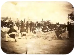 Une vieille photo montrant une procession passant entre des rangées de soldats avec des tentes en toile de fond