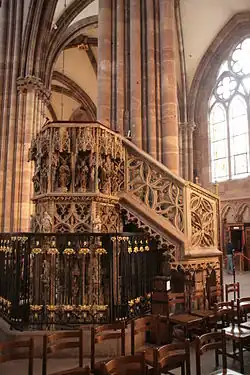 vue d’une chaire à prêcher en pierre adossée à un pilier et abondamment sculptée, avec des statues sous des dais gothiques