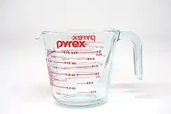 Verre doseur avec graduations et logo de la marque en rouge