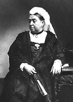 Photographie en noir et blanc d'une vieille femme en tenue de deuil, tenant dans ses mains un éventail.
