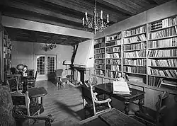 Photographie d'un salon bourgeois avec de grandes étagères remplies de livres.