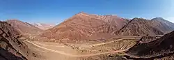 Une vallée encaissée, des montagnes arides à la roche striée de rouge, d'ocre et de brun, un train filant le long de canaux d'irrigation.