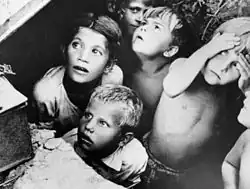 Photo noir et blanc montrant des visages d'enfants en gros plan, visiblement appeurés. Ils ont l'air de se cacher, mais on ne distingue pas leurs alentours.