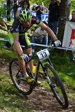 Homme descendant une pente à VTT, portant une tenue verte et noire.