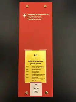 Photographie d'un classeur rouge avec étiquette jaune contenant le volume 0.1 du Recueil systématique en langue française