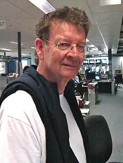 Photo d'un homme blanc aux cheveux courts et frisés portant des lunettes.