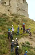 Remblaiement de la motte castrale par un groupe de bénévoles formant une chaîne.