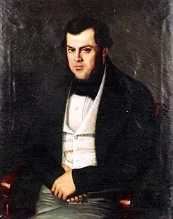 Tableau représentant un homme assis portant une veste noire, une chemise blanche, il a les mains croisées sur son ventre.