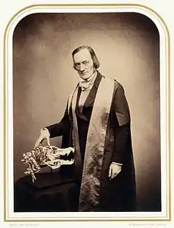 Photographie d'un homme de trois quarts, une main posée sur un crâne.