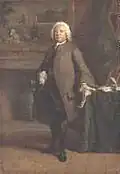 Portait en pied. Personnage en costume XVIIIe : perruque blanche, culotte noire, redingote marron, devant une cheminée, main droite glissée dans le gilet, main gauche tenant une lettre appuyée sur une table avec une écritoire