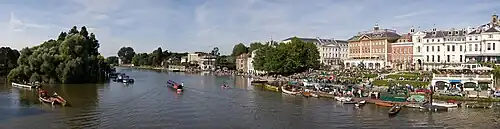 Photo. Large fleuve avec embarcation et à droite rive arborée avec larges terrasses et façades classiques