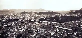 Vue plongeante sur les toits d'une grande ville avec des collines et un cours d'eau dans le lointain