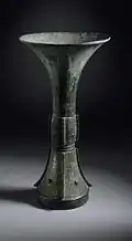 Photo d'un vase vertical, de couleur noire-verte, ayant une forme d'entonnoir allongé.