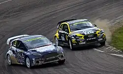À l'intérieur d'un virage, la voiture jaune et noire de Larsson tente de doubler la voiture blanche et bleue de Bakkerud