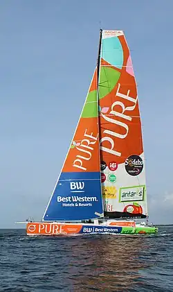Voilier orangé, bleu et vert en mer, vu en entier, de profil.
