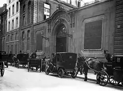 Des fiacres et une automobile garés devant une porte cochère portant au fronton l'inscription CREDIT FONCIER DE FRANCE.
