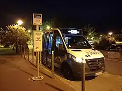 Photographie nocturne en couleurs d’un minibus bleu, blanc et noir stationné à un arrêt de bus