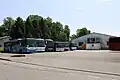 Photographie en couleurs de plusieurs bus multicolores stationnés côte-à-côte devant un batiment gris, en arrière plan à droite : le dépôt d’Albanais Voyages