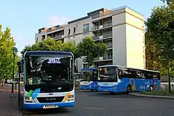 Photographie en couleurs de trois cars devant un immeuble résidentiel, deux du réseau de Rumilly en arrière-plan et un du réseau d’Annecy au premier plan.