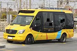 Photographie en couleurs d’un minibus jaune et noir, avec des installations ferroviaires en arrière-plan.