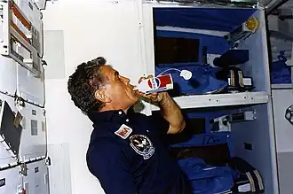 Karl Henize boit dans une canette de Pepsi