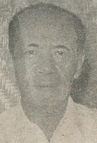 Portrait en noir et blanc d'un homme asiatique à la peau foncée, vêtu d'une chemise claire. Il est centré, avec une expression neutre et un regard dirigé vers l'observateur. L'image, légèrement floue et granuleuse, a un arrière-plan neutre et un éclairage diffus. L'atmosphère est sobre, évoquant un portrait officiel ancien.