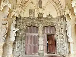Photographie d'un intérieur de porche d'église, avec des parties en granite, d'autres en calcaire et des statues d'apôtres.