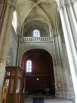 Chapelle avec une peinture murale rouge, surmontée par une tribune ouverte sur le collatéral nord. À droite, l'une des entrées de la basilique est visible.
