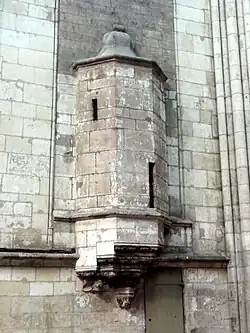 Échauguette en encorbellement avec un toit de pierre ressemblant à une cloche. En bas à droite, une vieille porte en bois.